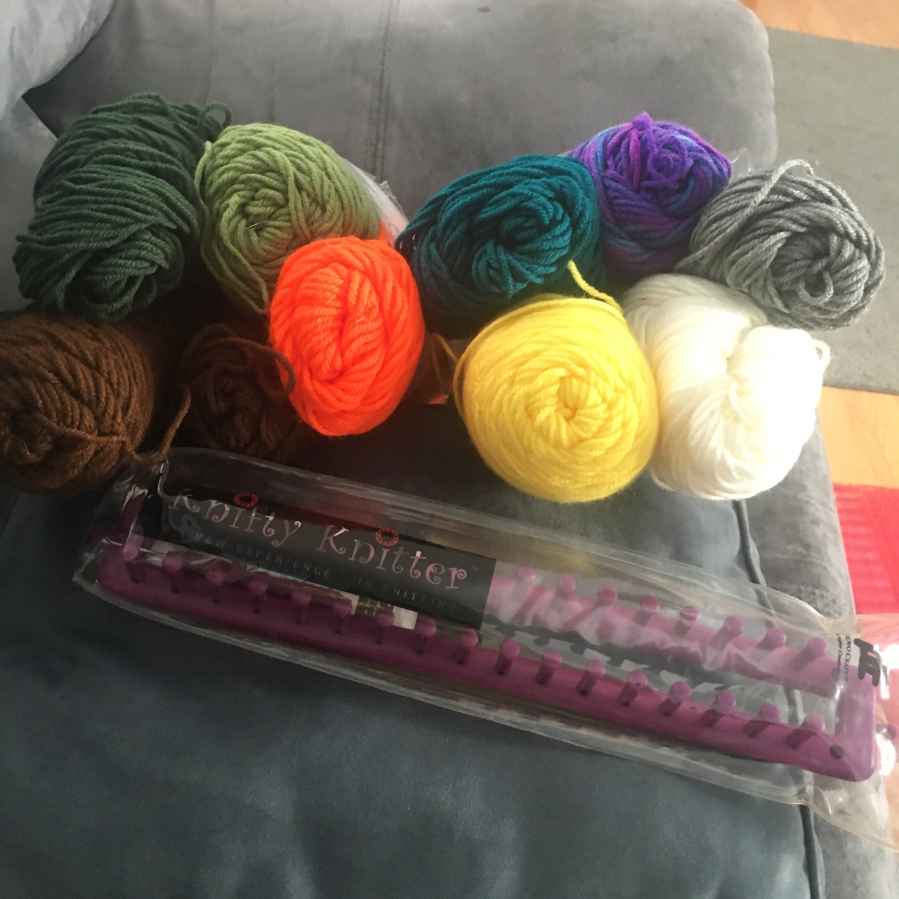 The ends of 10 skeins of basic 4-ply yarn, stacked on top of one another like logs, each a different bright or dark color. In front of the yarn, a rake, or rectangular loom.