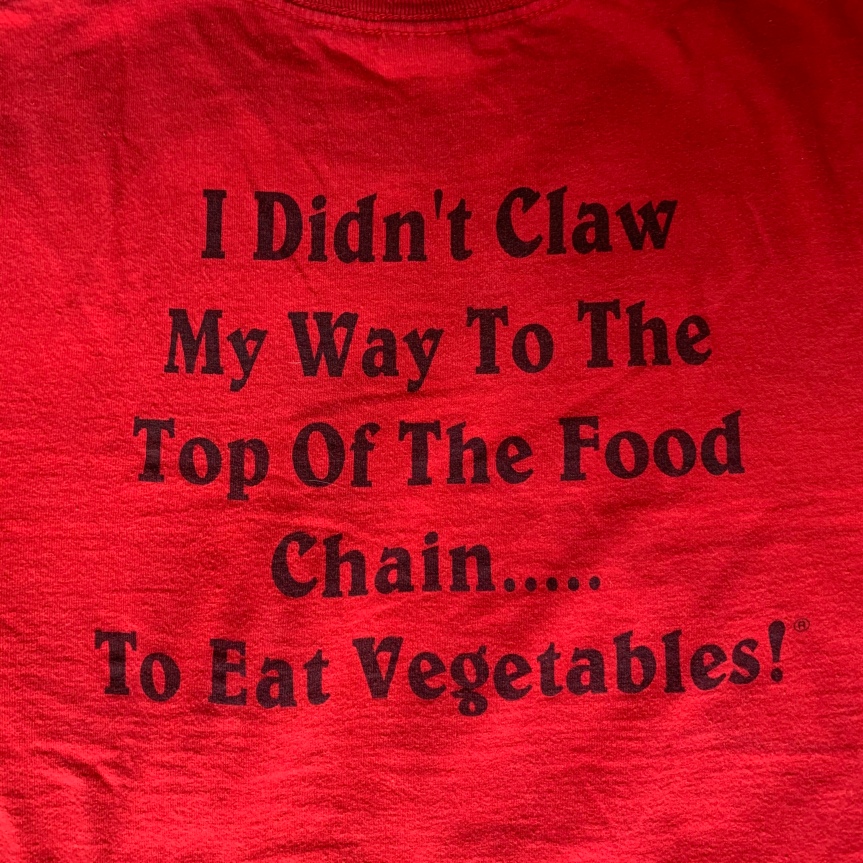Close up of slogan on back of Rudy’s T-shirt, black print on red, that reads: “I didn’t claw my way to the top of the food chain to eat vegetables.“